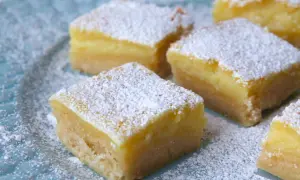 Färska bitar av citronkaka i långpanna, pudrade med florsocker, ligger på en blå tallrik.
