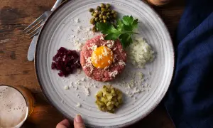 En tallrik med råbiff, äggula, kapris, hackad lök, rödbetor och gurka. Perfekt för ett klassiskt råbiff recept.