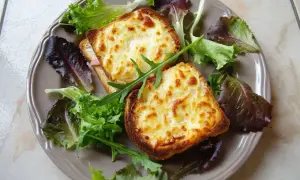 Två gyllene croque monsieur med smält ost och en fräsch sallad på en tallrik.