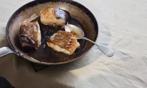 Stekt kolja i en panna, perfekt för ett enkelt kolja recept. En sked ligger bredvid fisken.