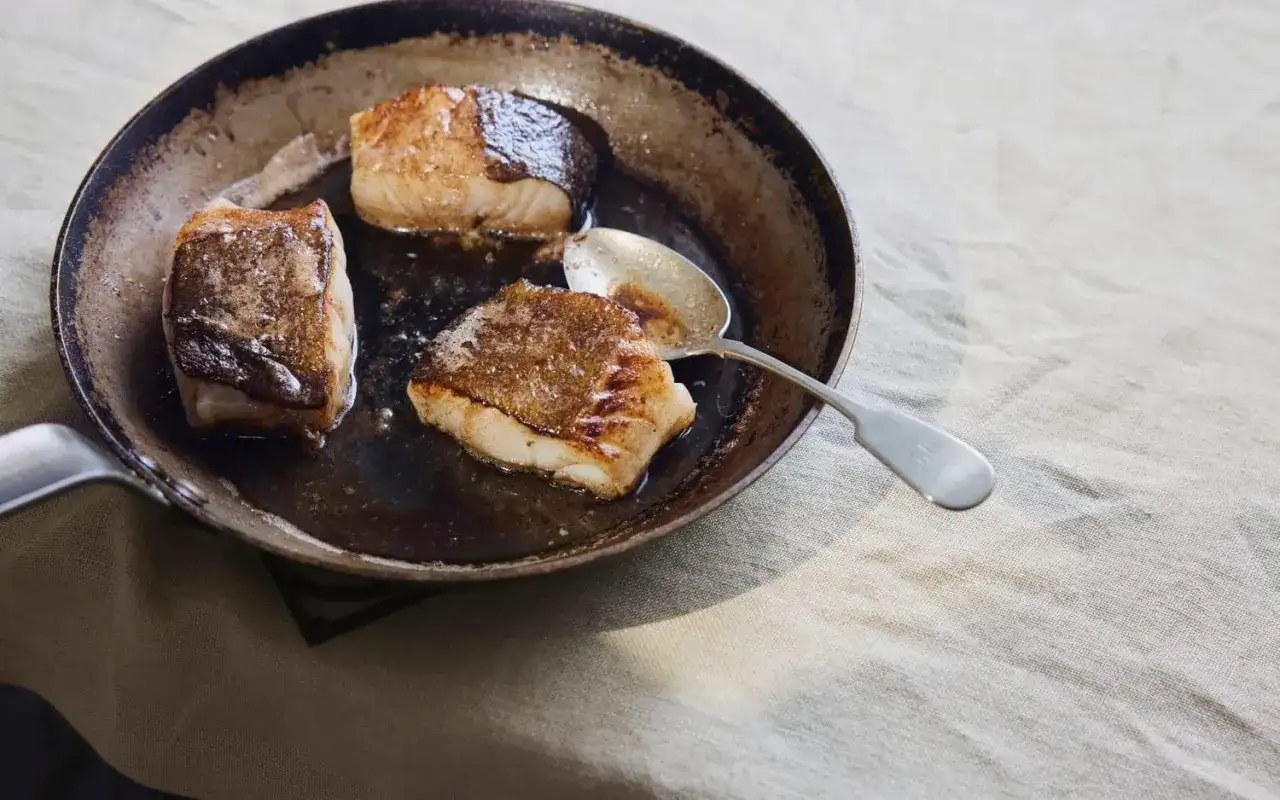 Stekt kolja i en panna, perfekt för ett enkelt kolja recept. En sked ligger bredvid fisken.