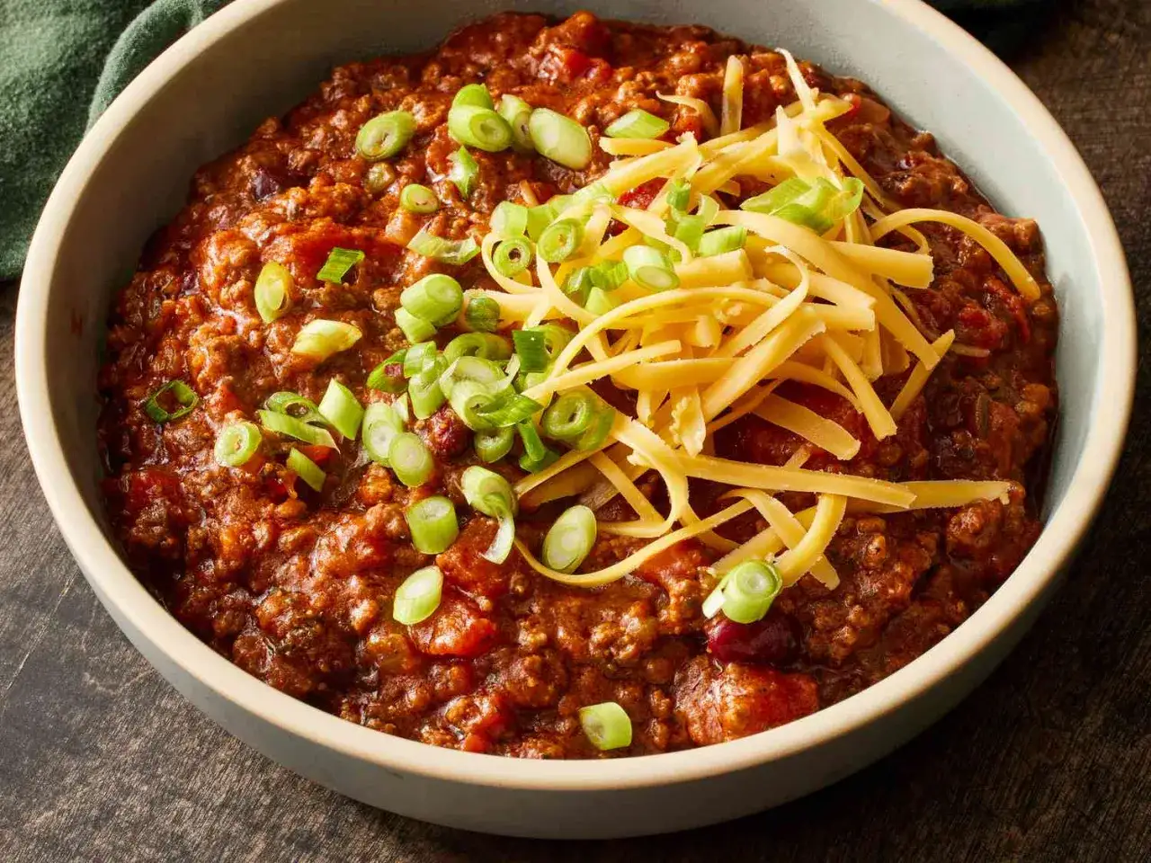 En skål med mustig chili con carne, toppad med riven ost och färsk salladslök. Perfekt för en kall kväll.