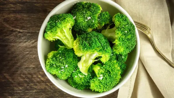 En skål med nykokt, grön broccoli, strödd med flingsalt. En gaffel ligger bredvid på en beige duk.