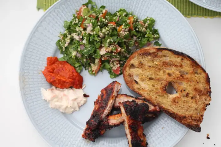 En tallrik med grillade revbensspjäll, rostat bröd, en krämig sallad och en fräsch tabbouleh. Perfekt för ett somrigt tabbouleh recept.